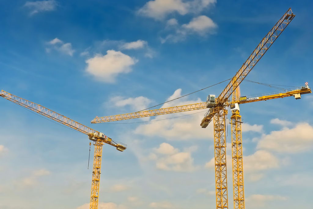 Gruas de construção civil em canteiro de obras, representando engenharia, infraestrutura e desenvolvimento imobiliário.